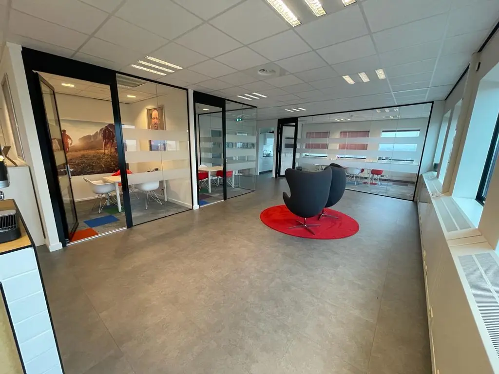 Moderne kantoorruimte met glazen vergaderruimtes en twee zwarte stoelen op een rood kleed op het Johanna Westerdijkplein.